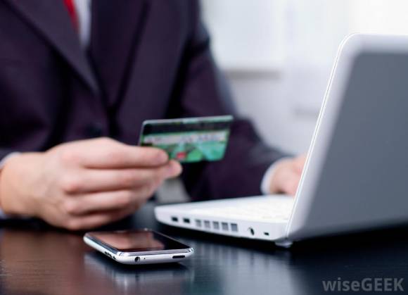 man with credit card at desk with phone and white computer